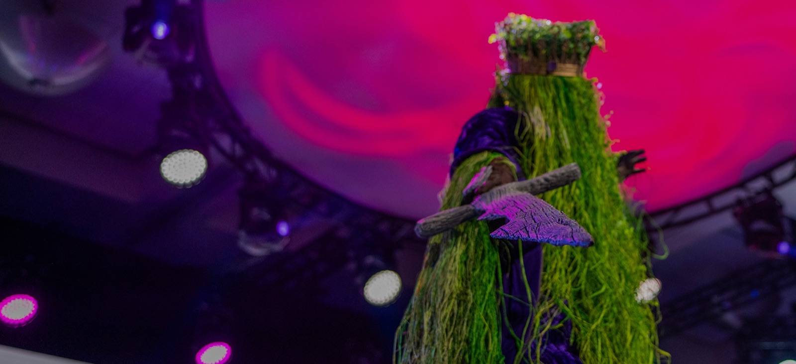 A cosplayer in a grass-covered costume on stage at TwitchCon